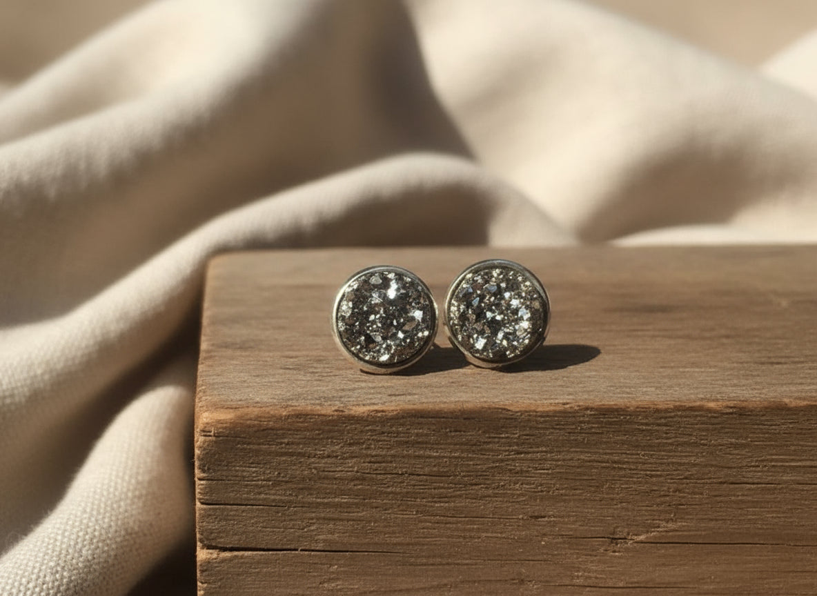 Silver druzy stud earrings on a wooden block with beige fabric background